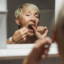 Woman flossing her teeth in bathroom mirror