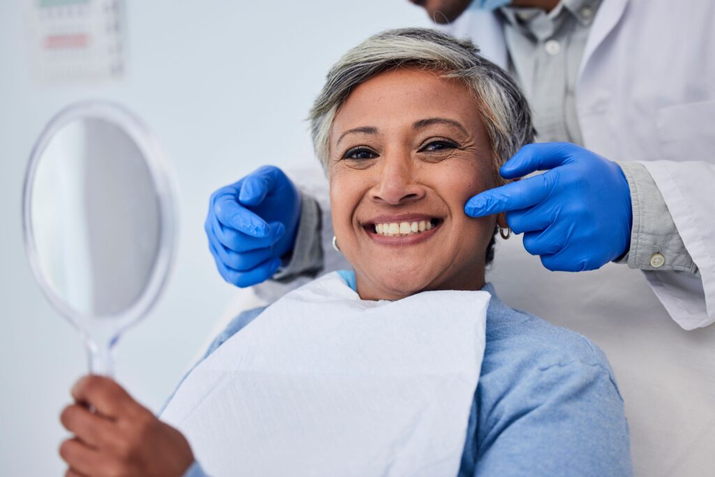 Woman with short grey hair smiling in dental chair with mirror